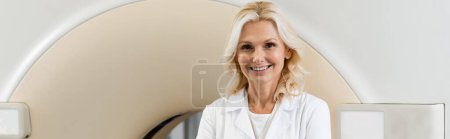 Photo for Middle aged radiologist smiling at camera near computed tomography machine, banner - Royalty Free Image