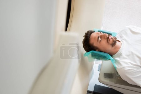 Besorgter Mann mit geschlossenen Augen liegt bei Untersuchung auf Scanner in Klinik