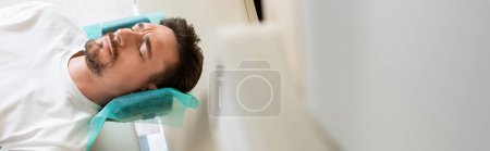 worried man with closed eyes doing computed tomography in hospital, banner