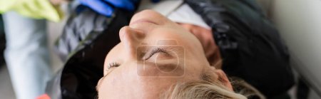 Photo for Middle aged woman lying near blurred paramedic in emergency vehicle, banner - Royalty Free Image