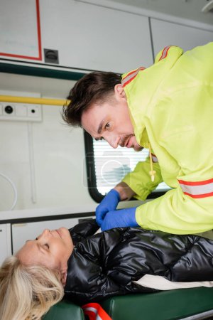 Paramedic in latex gloves giving first aid to unconscious middle aged woman in emergency vehicle 