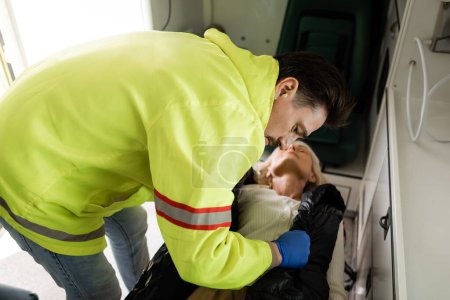 Paramédico en uniforme quitando chaqueta de paciente inconsciente en coche de emergencia 