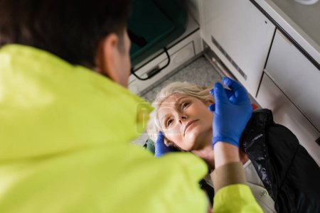 Vista de ángulo alto de paramédico borroso en guantes de látex dando primeros auxilios al paciente en vehículo de emergencia 