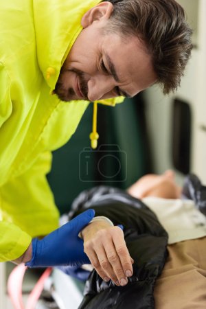 Focused paramedic checking pulse of blurred woman in emergency vehicle 