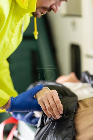 Ausgeschnittene Ansicht des Sanitäters, der den Puls einer verschwommenen Frau im Einsatzfahrzeug überprüft 