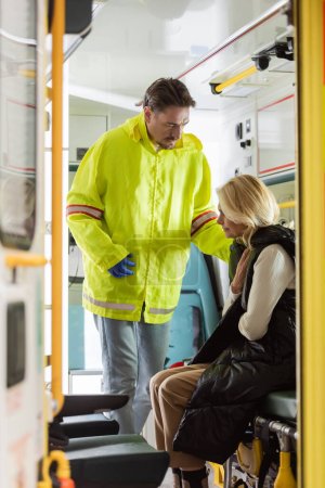 Paramédico en uniforme mirando al paciente enfermo en vehículo de emergencia 