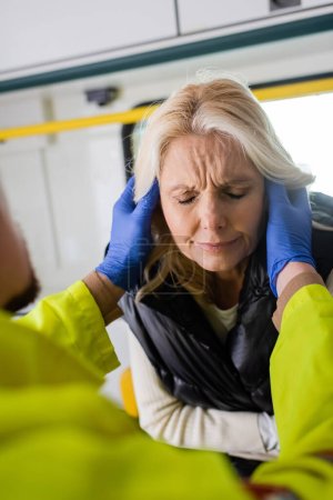 Paramedic giving first aid to middle aged woman suffering from pain in emergency vehicle 