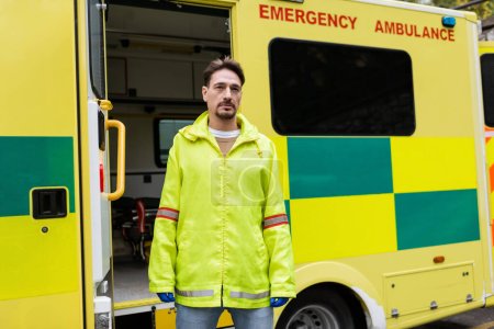Paramedic in latex gloves standing near ambulance car outdoors 