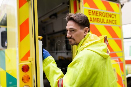 Paramedic standing near blurred ambulance car with open door outdoors 