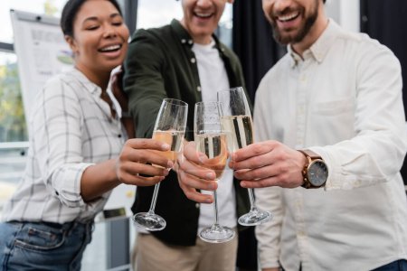 Des hommes d'affaires multiethniques flous décrochent du champagne lors d'une fête d'entreprise au bureau 