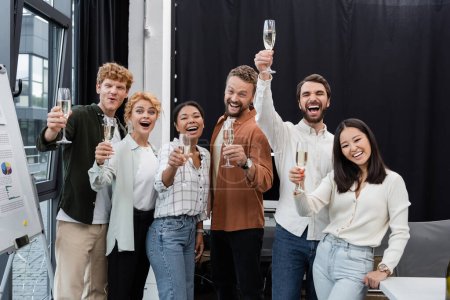 Téléchargez les photos : Des gens d'affaires multiculturels excités montent des verres de champagne au bureau - en image libre de droit