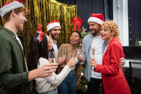 Photo for Excited multicultural business people in santa hats clinking champagne in office - Royalty Free Image