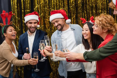 Positive interracial business people holding champagne during Christmas corporate party in office 