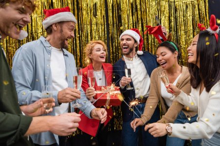 Excited multiethnic business people holding champagne and sparklers during Christmas party in office 