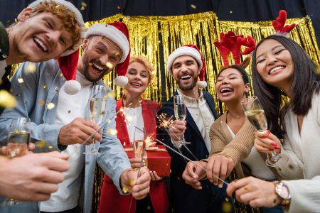 Niedriger Blickwinkel auf multiethnische Geschäftsleute mit Wunderkerzen und Champagner während der Neujahrsparty im Amt 