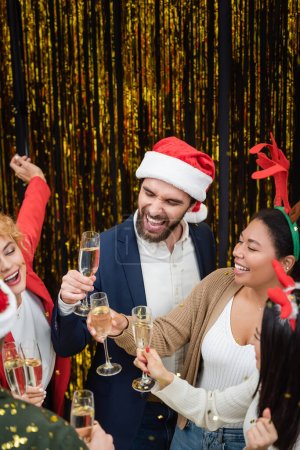Foto de Gente de negocios interracial con champán bailando bajo confeti durante la fiesta de Año Nuevo en la oficina - Imagen libre de derechos