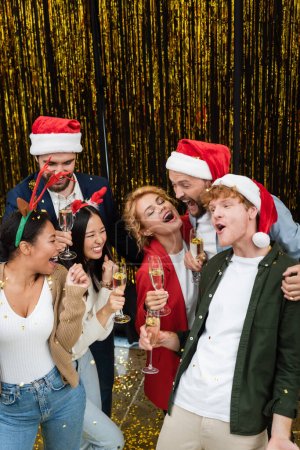 High angle view of excited multiethnic business people with champagne dancing near tinsel in office 