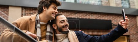 bearded gay man taking selfie with boyfriend holding shopping bag outdoors, banner