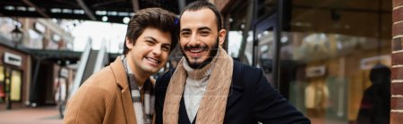 joyeux gay partenaires dans foulards et manteaux regardant caméra sur la rue de la ville, bannière
