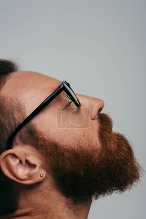 Photo for Side view of bearded man in eyeglasses closing eye isolated on grey - Royalty Free Image
