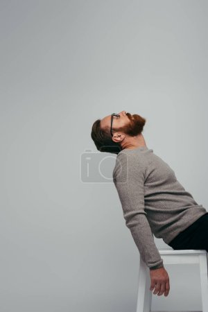Photo for Side view of stylish man in long sleeve sitting on chair isolated on grey - Royalty Free Image