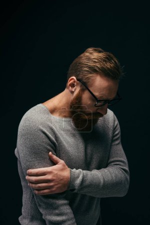 Stilvoller aufgebrachter Mann mit Brille berührt Arm isoliert auf Schwarz 