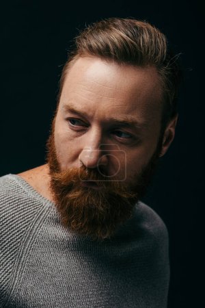 Portrait of bearded man in grey jumper looking away isolated on black 