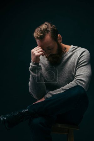 Trauriger Mann in grauem Langarm sitzt isoliert auf schwarzem Stuhl 