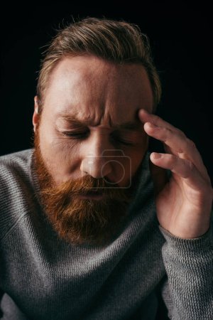 Porträt eines besorgten Mannes mit langem Ärmel, der Stirn isoliert auf Schwarz berührt 