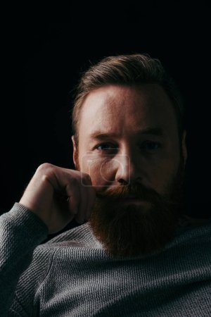 Portrait d'homme barbu regardant la caméra isolée sur noir avec ombre 