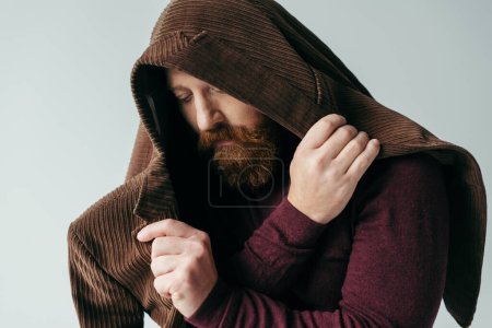 hombre barbudo con chaqueta marrón en la cabeza posando aislado en gris 