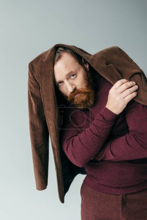 Photo for Bearded man with brown blazer on head and burgundy turtleneck looking at camera isolated on grey - Royalty Free Image