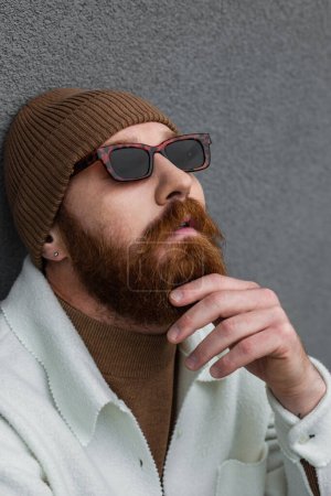 Porträt eines bärtigen Hipsters mit stylischer Sonnenbrille und trendigem Hut, der wegschaut