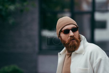 bearded hipster in stylish sunglasses and white shirt jacket looking away 