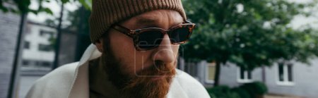 suspicious man with beard in stylish sunglasses and beanie hat, banner