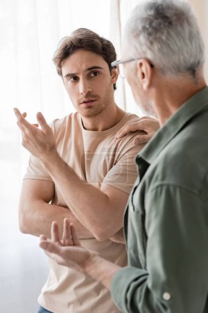 Photo for Mature man touching shoulder and talking to upset son on blurred foreground - Royalty Free Image