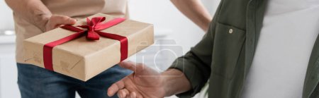 cropped view of man holding gift box with red ribbon near dad on fathers day, banner