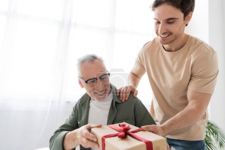 Junger Mann übergibt Geschenkbox an glücklichen Vater, während er ihm zum Vatertag gratuliert