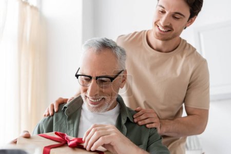 smiling man touching shoulders of happy dad opening fathers day present