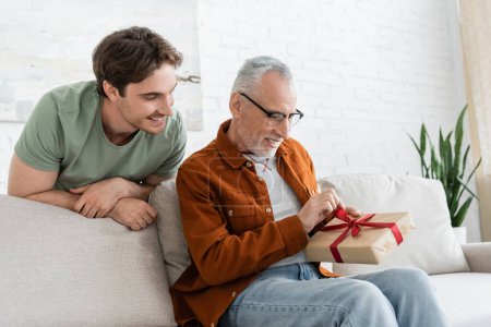 young man smiling near pleased dad opening present on fathers day