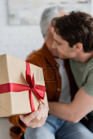 selektiver Fokus der Geschenkbox mit roter Schleife in der Nähe eines verschwommenen Mannes, der Papa am Vatertag umarmt