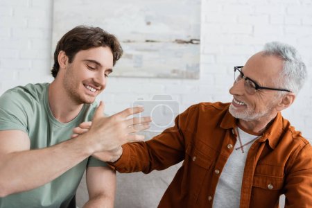 fröhlicher bärtiger Mann mit Brille gibt High Five an glücklichen Sohn zu Hause