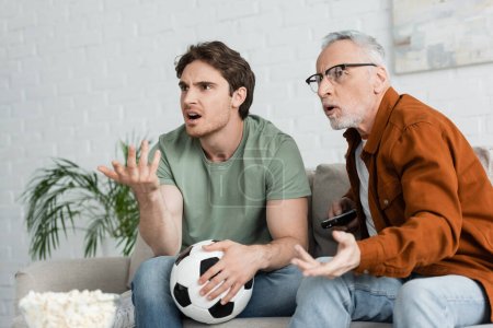 Unzufriedener Vater und Sohn zeigen mit den Händen auf Fußballmeisterschaft im Wohnzimmer