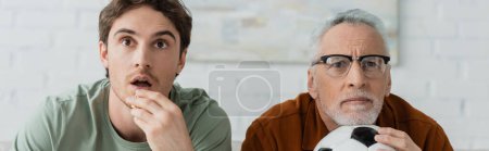 mature and worried man with soccer ball watching football championship near tensed son at home, banner