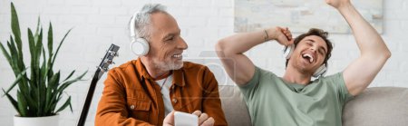 Mature man in wireless headphones holding smartphone and looking at singing son, banner