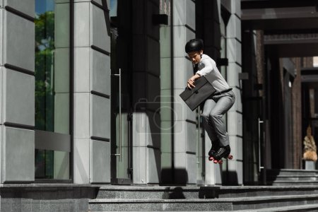 Businessman in roller skates jumping and holding briefcase while riding on urban street 