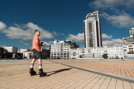 Téléchargez les photos : Vue latérale de l'homme en patins à roulettes tenant téléphone portable et café à emporter dans la rue urbaine - en image libre de droit