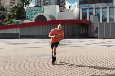 Téléchargez les photos : Jeune patineuse à roulettes avec smartphone et café pour rouler dans la rue urbaine - en image libre de droit