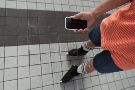 Top view of roller skater holding smartphone with blank screen outdoors 