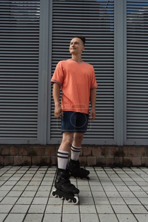 Jeune homme en vêtements décontractés et patins à roulettes debout sur la rue urbaine 